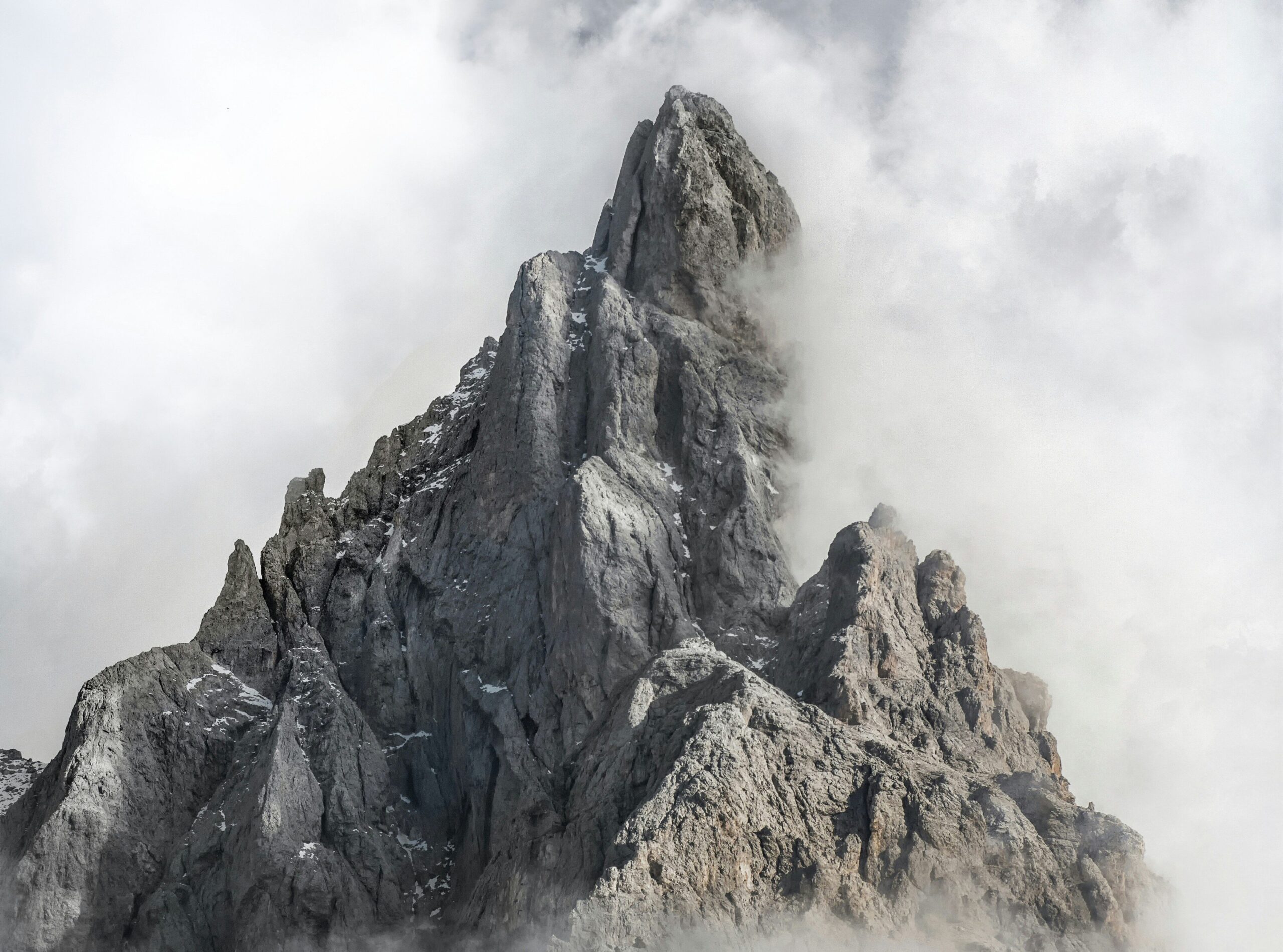 A person stands on a grassy hill below a misty, jagged mountain peak.